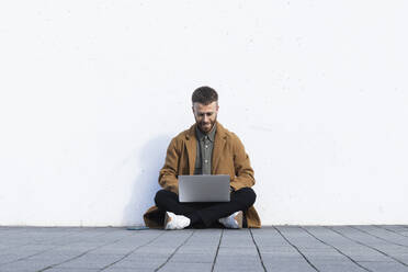 Mid adult businessman working on laptop while sitting on footpath - PNAF00797