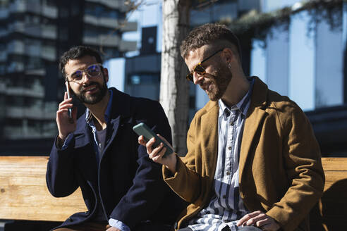 Geschäftsleute benutzen Mobiltelefone, während sie auf einer Bank sitzen - PNAF00809