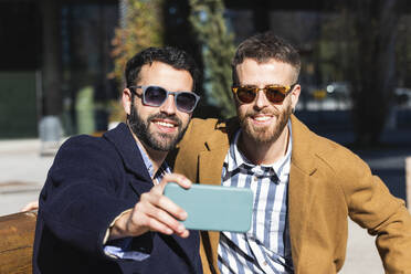 Smiling business partners taking selfie through mobile phone while sitting outdoors - PNAF00810