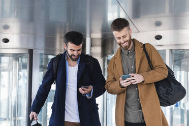 Geschäftspartner, die Mobiltelefone benutzen, während sie mit der Tasche am Gebäude stehen - PNAF00818