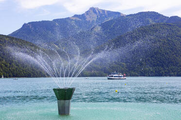 Springbrunnen am Ufer des Wolfgangsees im Sommer mit dem bewaldeten Schafberg im Hintergrund - WWF05762