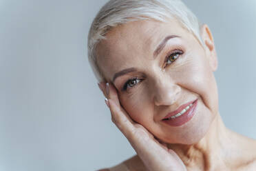 Senior woman smiling while standing against gray background - OIPF00381