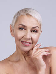 Smiling senior woman looking away while standing against gray background - OIPF00385