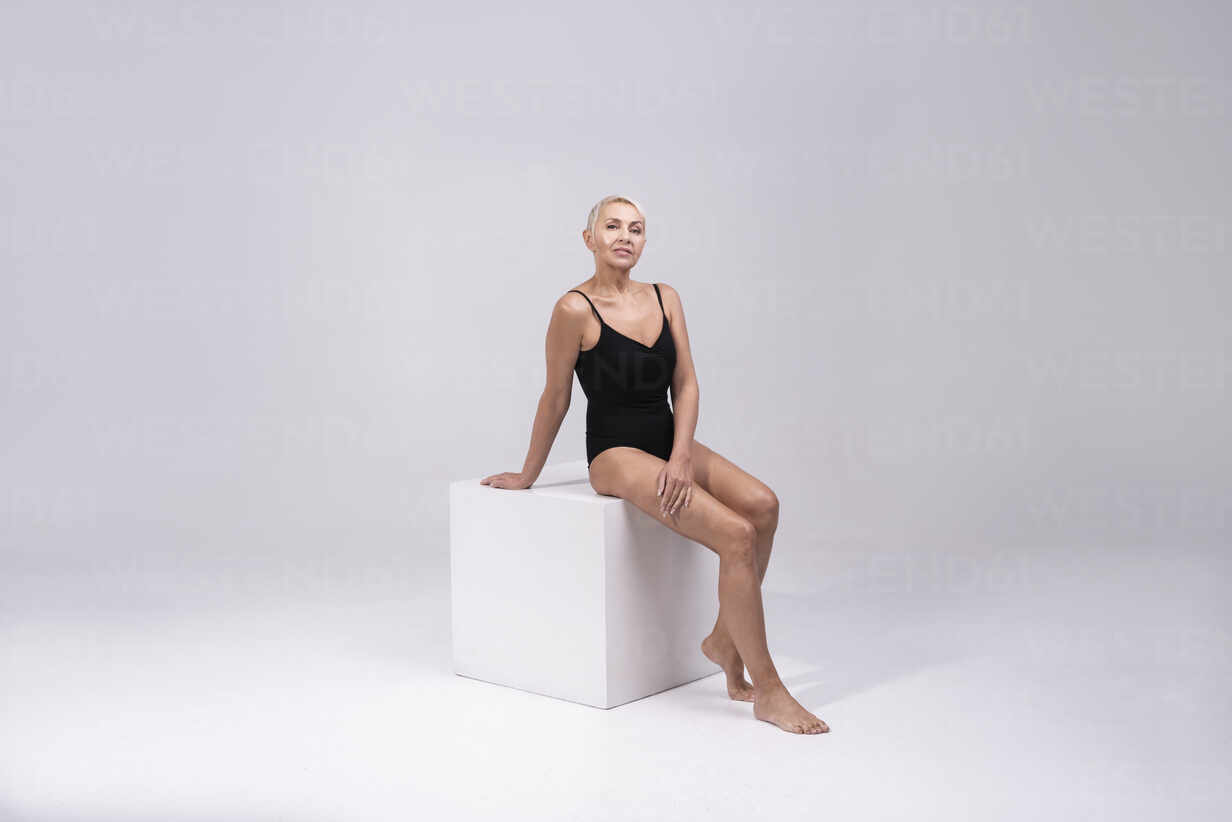 Fit Naked Woman Sitting on White Cube in Studio Stock Photo