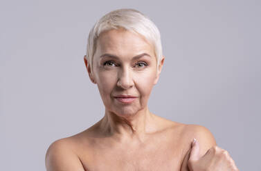 Ältere Frau starrt im Stehen vor grauem Hintergrund - OIPF00409