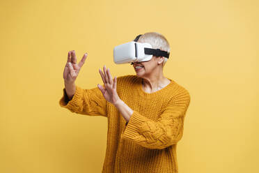 Frau gestikuliert, während sie ein Virtual-Reality-Headset vor einem gelben Hintergrund benutzt - OIPF00421