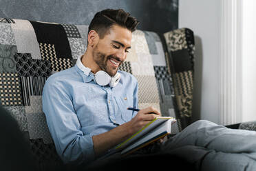 Mittlerer erwachsener Mann, der lächelnd in ein Buch schreibt und zu Hause sitzt - EGAF01945