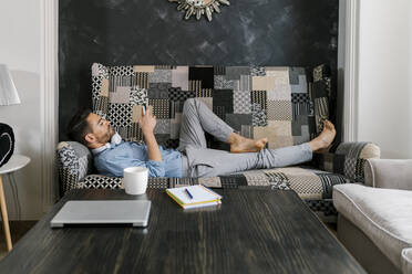Man using mobile phone while relaxing on sofa at home - EGAF01948