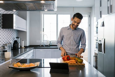 Smiling man with vegetables standing at kitchen counter - EGAF01952