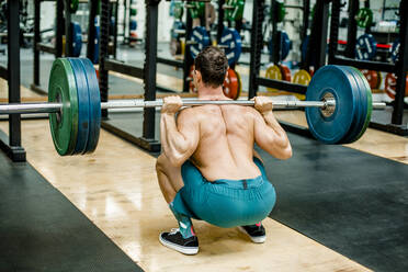Mann in hockender Position beim Gewichtheben im Fitnessstudio - KVF00169