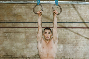 Mann hält Gymnastikringe gegen die Wand eines Fitnessstudios - KVF00172