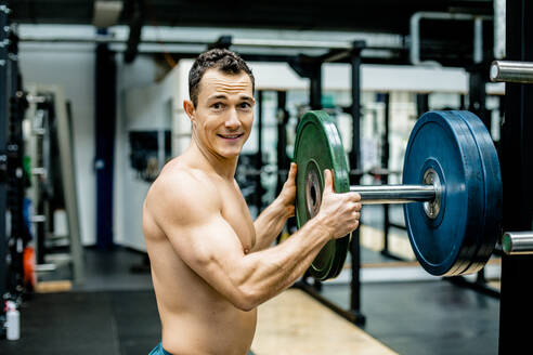 Lächelnder Sportler ohne Hemd, der Gewichte in einem Fitnessstudio hält - KVF00174