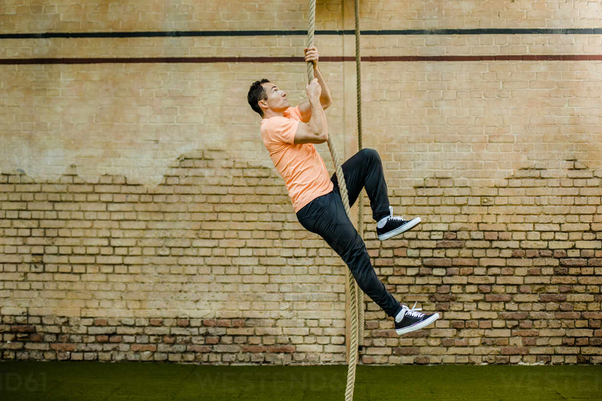 Man climbing on rope by brick wall at gym stock photo