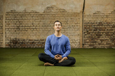 Man meditating against wall in health club - KVF00197