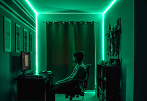 Jugendlicher spielt ein Videospiel am Schreibtisch in einem Raum mit Neon-LED-Beleuchtung. - CAVF93545