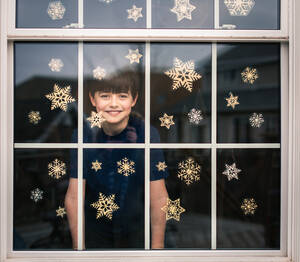 Fröhlicher Junge, der durch ein mit Schneeflocken bedecktes Fenster hinausschaut. - CAVF93549