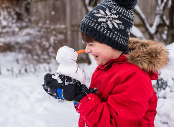 Junge hält an einem verschneiten Tag im Freien einen kleinen Schneemann in den Händen. - CAVF93553