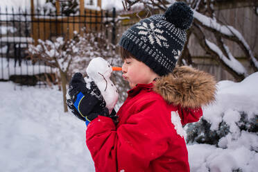 Junge hält an einem verschneiten Tag im Freien einen kleinen Schneemann in den Händen. - CAVF93554