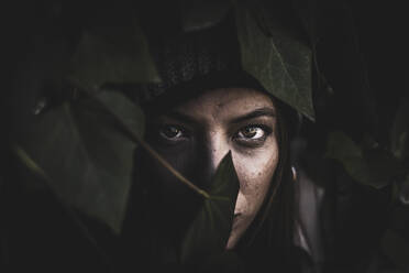Porträt eines rothaarigen Mädchens mit Farnblättern, die ihr Gesicht teilweise bedecken - CAVF93568
