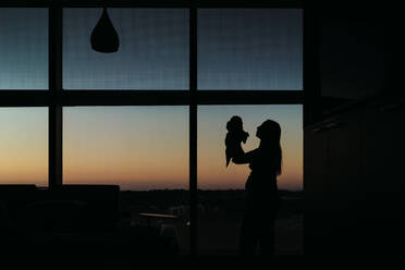 Silhouette von Mutter und Neugeborenem im Krankenhauszimmer bei Sonnenuntergang - CAVF93573