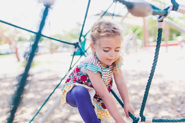 Junges blondes Mädchen spielt auf einem öffentlichen Spielplatz an einem sonnigen Tag. - CAVF93587