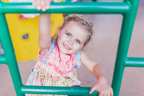 Mädchen im Vorschulalter mit großen blauen Augen spielt auf einem öffentlichen Spielplatz. - CAVF93589