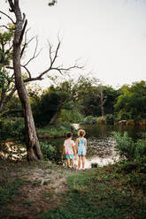 Junger Bruder und junge Schwester starren im Sommer ins Wasser eines Sees - CAVF93601