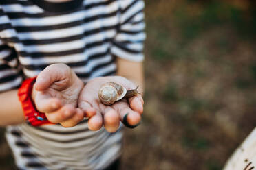 Close up of young boy outside holding snail in dirty hands - CAVF93606