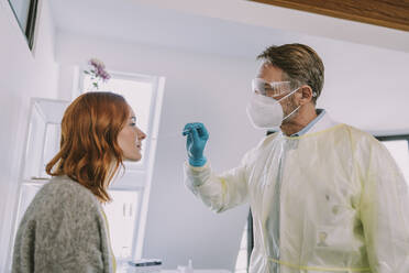 Doctor in protective suit and face mask checking patient while standing in examination room - MFF07389