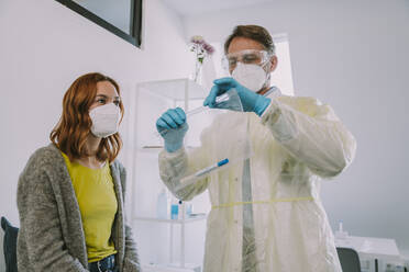 Doctor packaging patient's nasal swab sample in plastic bag while standing by patient at examination room - MFF07395