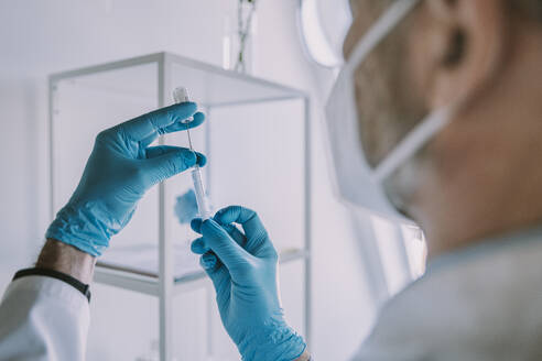 Doctor taking vaccination in syringe while standing at examination room during COVID-19 - MFF07396