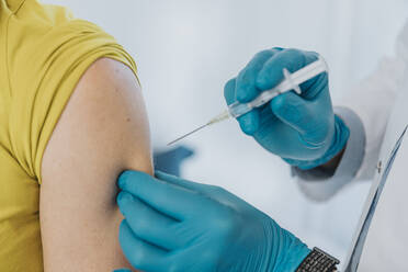 Arzt verabreicht COVID-19-Impfstoff an Patientenhand im Untersuchungsraum - MFF07401