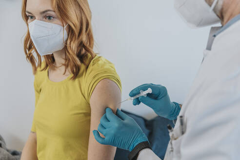 Doctor injecting COVID-19 vaccination on patient hand while standing at examination room - MFF07402