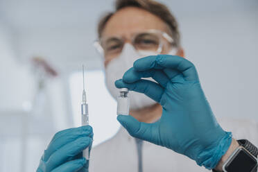 Healthcare worker holding COVID-19 vaccination vial and syringe at examination room - MFF07403