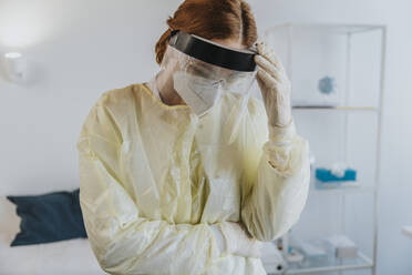Female healthcare worker wearing protective workwear standing with hand in hand at examination room - MFF07405