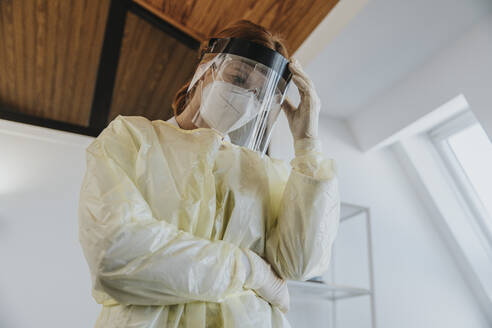 Female doctor wearing protective workwear standing with hand in hand at examination room - MFF07406