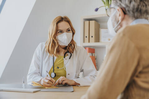 Arzt mit Schutzmaske, der im Büro sitzend den Impfpass eines Patienten unterzeichnet, lizenzfreies Stockfoto