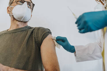 Arzt mit Spritze desinfiziert den Arm eines Patienten, während er im Untersuchungsraum steht - MFF07427