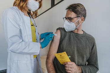 Female doctor putting adhesive bandage on patient arm while standing at examination room - MFF07437