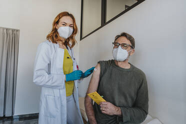Arzt mit Schutzmaske, der einen Verband anlegt, während er bei einem männlichen Patienten im Untersuchungsraum steht - MFF07438