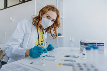 Arzt mit Gesichtsschutzmaske, der im Untersuchungsraum eine Probe auf Testkassetten untersucht - MFF07449