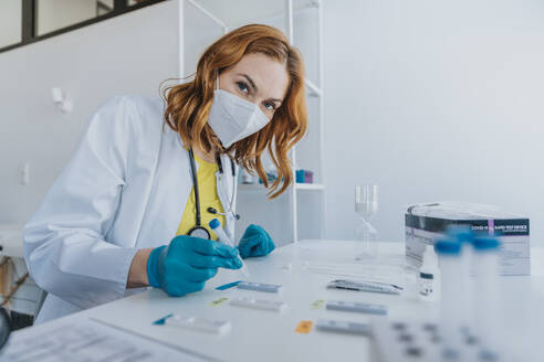 Doctor wearing protective face mask testing sample on test cassettes at examination room - MFF07449