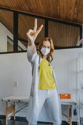 Doctor gesturing victory sign while standing in clinic - MFF07466