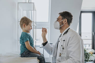 Pediatrician wearing protective face mask taking nasal swab test of boy while standing at clinic - MFF07468