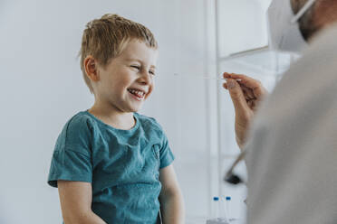 Junge lächelt bei einem Nasenabstrich, der von einem Arzt in einer Klinik durchgeführt wird - MFF07469