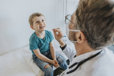 Doctor taking nasal swab test of boy while sitting at clinic - MFF07470