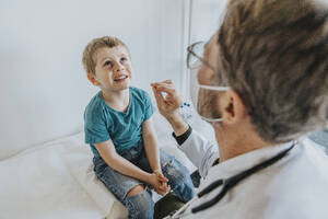 Arzt, der einen Nasenabstrich bei einem Jungen macht, während er in der Klinik sitzt - MFF07470