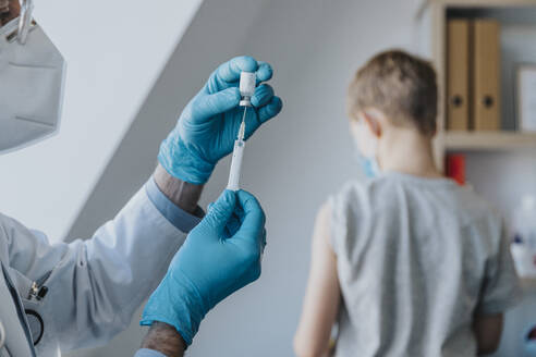 General Practitioner preparing vaccine in syringe for patient at clinic - MFF07480