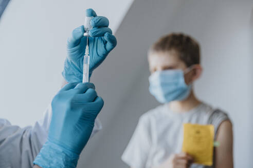 Arzt füllt Spritze mit COVID-19-Impfstoff für den Jungen im Hintergrund in der Klinik - MFF07482