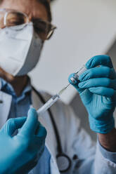 Male general practitioner filling syringe with COVID-19 vaccine while standing at clinic - MFF07486